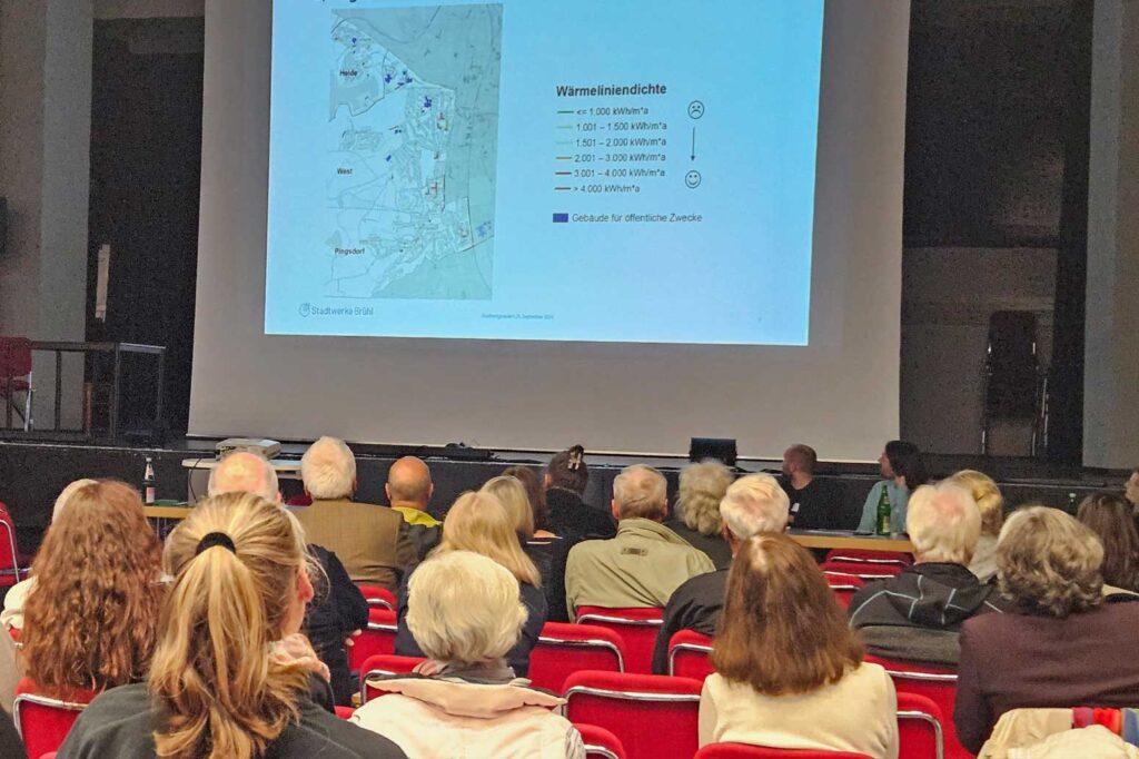 Zuhörer sitzen in einem Saal und blicken auf eine Präsentation