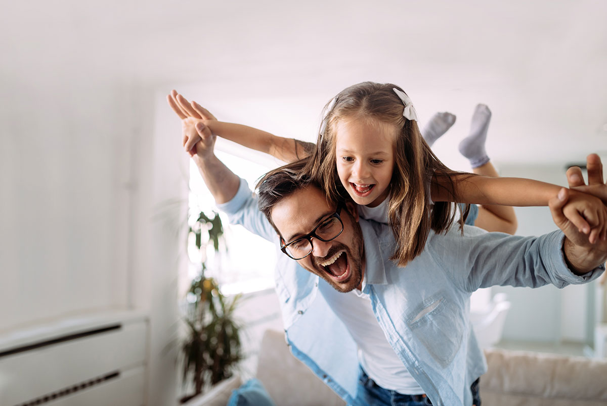 Vater macht im Wohnzimmer den Flieger mit Tochter