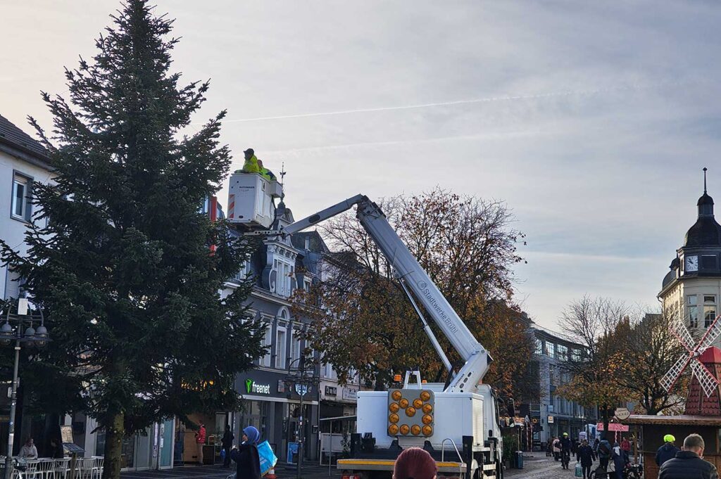 zwei Stadtwerke Mitarbeiter auf dem Hubwagen schmücken den Baum