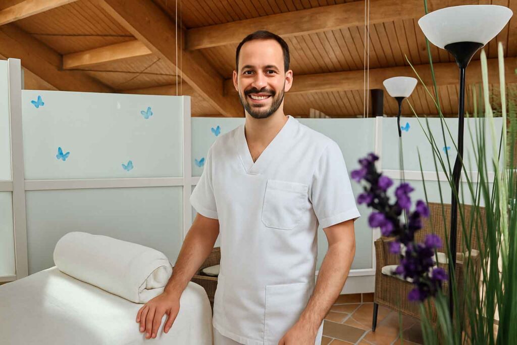 Masseur steht fröhlich neben Massageliege