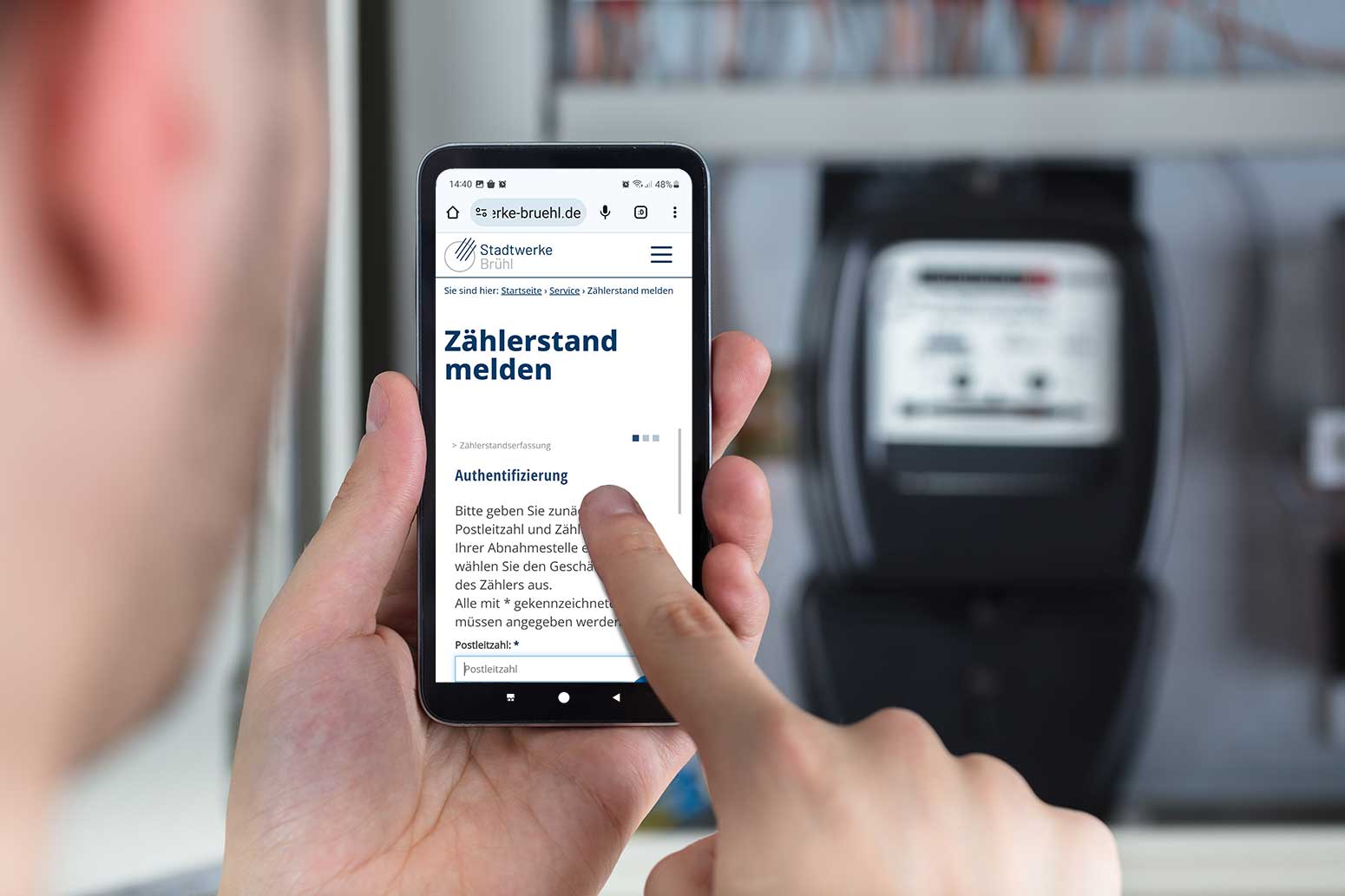 Person mit Smartphone vor dem Stromzähler