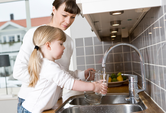 Kind mit Mutter füllen Glas an Wasserhahn auf